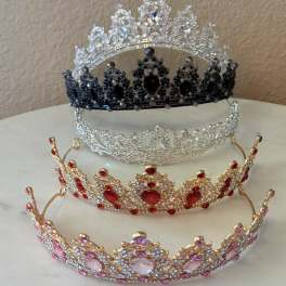 Four jeweled tiaras in silver, black, red, and pink sit stacked on a table.