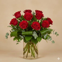 Red roses arranged in a clear glass vase with greenery