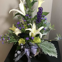 White lilies and purple flowers in a vase with a glittery purple "BOO" pick