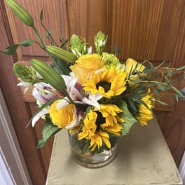 Bouquet of yellow sunflowers, roses, and lilies in a glass vase