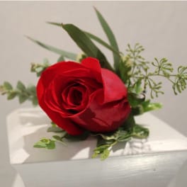 Single red rose boutonniere resting on a white surface