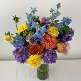Mixed bouquet of blue, purple, yellow, and peach flowers in a glass vase