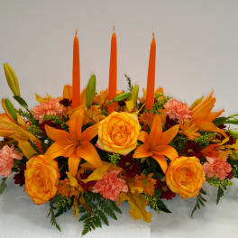 Orange floral centerpiece with roses, lilies, carnations, and tall candles