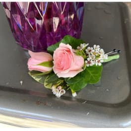 Pink rose boutonniere with small white blossoms and pins on a gray surface