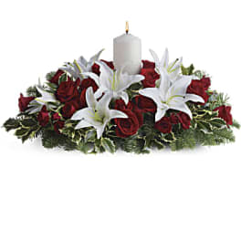 Red roses and white lilies arranged around a white candle