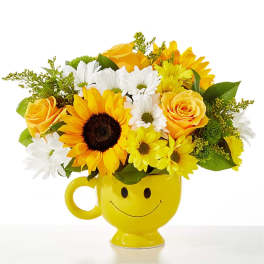 Yellow smiley-face mug holding a bouquet of sunflowers, roses, and daisies