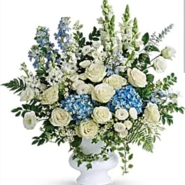White roses and blue flowers arranged in a white pedestal vase