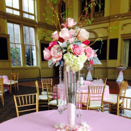 Tall pink and white floral centerpiece in a mirrored vase on a pink tablecloth