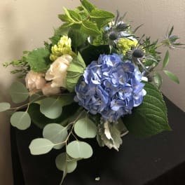 Bouquet of blue hydrangea, pale roses, and thistle in a vase