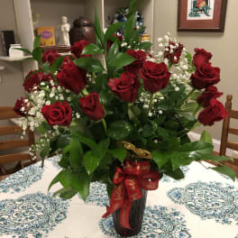 Red roses arranged in a tall black vase with baby's breath and a red ribbon