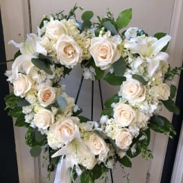Heart-shaped floral wreath of white roses and lilies on a stand