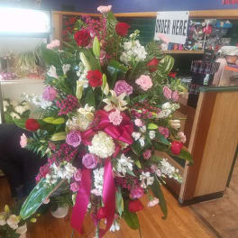 Large standing floral spray with roses, lilies, and pink ribbon
