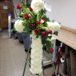 Standing floral cross with white blooms and red roses on an easel