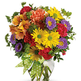 Mixed bouquet of colorful flowers in a clear glass vase with a green polka-dot ribbon