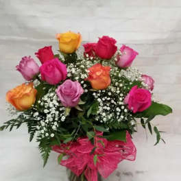 Bouquet of multicolored roses in a glass vase with pink ribbon