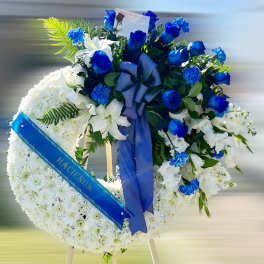 Standing white sympathy wreath with blue roses and ribbon on an easel