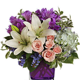 Bouquet of white lilies, pink roses, and purple flowers in a purple vase