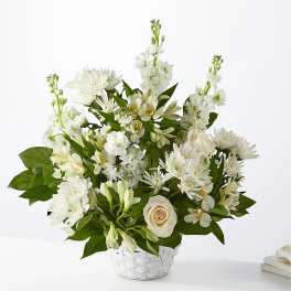 White floral arrangement in a white basket with roses and lilies