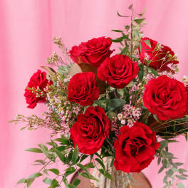 Red roses arranged in a gold vase with airy filler flowers