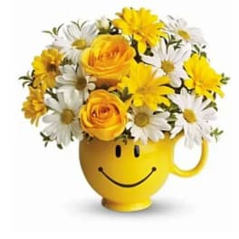 Yellow smiley-face mug holding yellow roses and white daisies