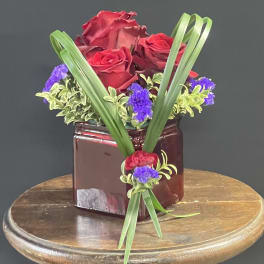 Red roses in a burgundy vase with purple accents and long green leaves