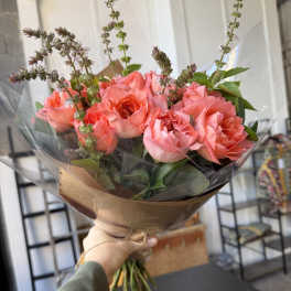 Handheld bouquet of pink roses wrapped in brown paper and clear plastic