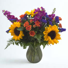 Bouquet of sunflowers, orange roses, and purple flowers in a green vase