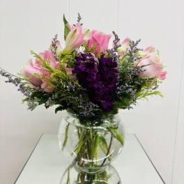 Pink lilies and purple flowers arranged in a clear glass vase