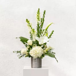White floral arrangement in a silver vase with tall green accents