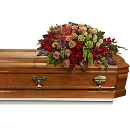 Casket spray with red and peach flowers on a wooden casket