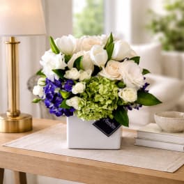 White and green floral arrangement in a square vase with purple blooms