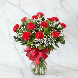 Red carnations and baby's breath in a glass vase with a red ribbon
