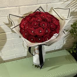 Bouquet of red roses wrapped in white paper with a black ribbon