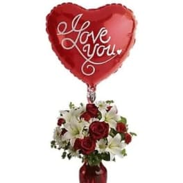 Heart-shaped red balloon above a vase of red roses and white lilies