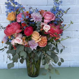 Mixed bouquet of roses, blue delphinium, and chrysanthemums in a glass vase