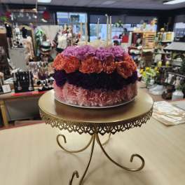 Round floral cake with pink, purple, and orange carnations and white candles
