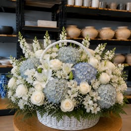 White basket arrangement with blue hydrangeas, white roses, and lilies