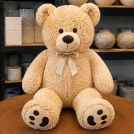 Large beige teddy bear with a ribbon bow sitting on a table