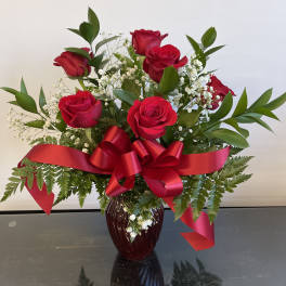 Red roses arranged in a vase with baby's breath and a red ribbon