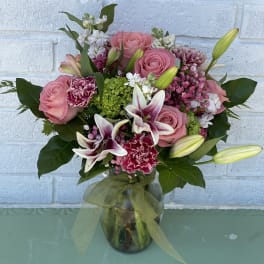 Pink roses and lilies arranged in a glass vase with a ribbon