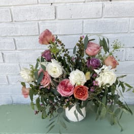 Mixed rose arrangement in a white vase with trailing greenery