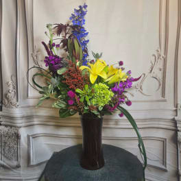 Tall mixed flower arrangement in a dark vase with yellow lilies and purple blooms