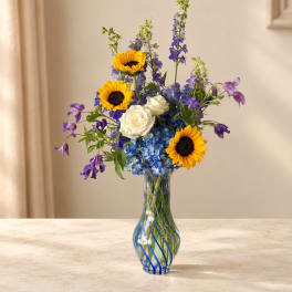 Sunflowers, white roses, and blue flowers in a striped glass vase