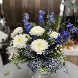 White chrysanthemums and blue flowers in a silver vase with a patterned ribbon