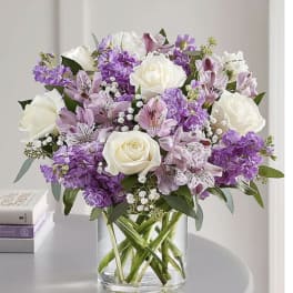 Bouquet of white roses and purple flowers in a clear glass vase