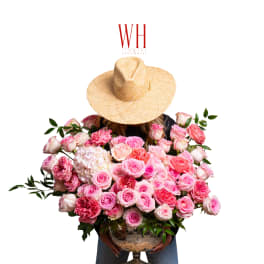 Large bouquet of pink roses in a glass vase held by a person wearing a straw hat.