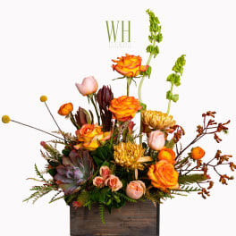 Mixed floral arrangement in a wooden box with orange roses and pale pink blooms