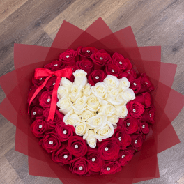 Round bouquet of red roses with a white heart of roses, wrapped in red paper with jewel accents