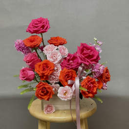 Bright pink and orange rose bouquet with a pink ribbon in a wooden box