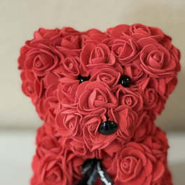 Red rose-covered teddy bear figurine with black eyes, nose, and ribbon
